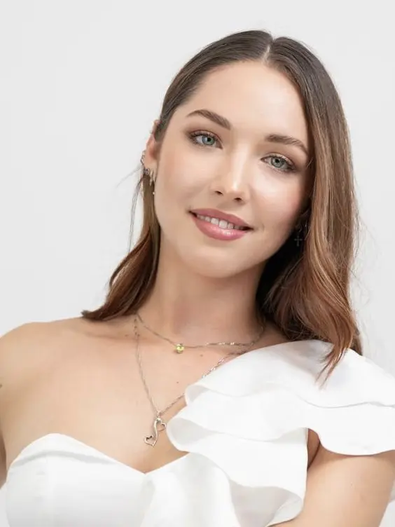 Smiling woman with light brown hair wearing a white off-shoulder top.
