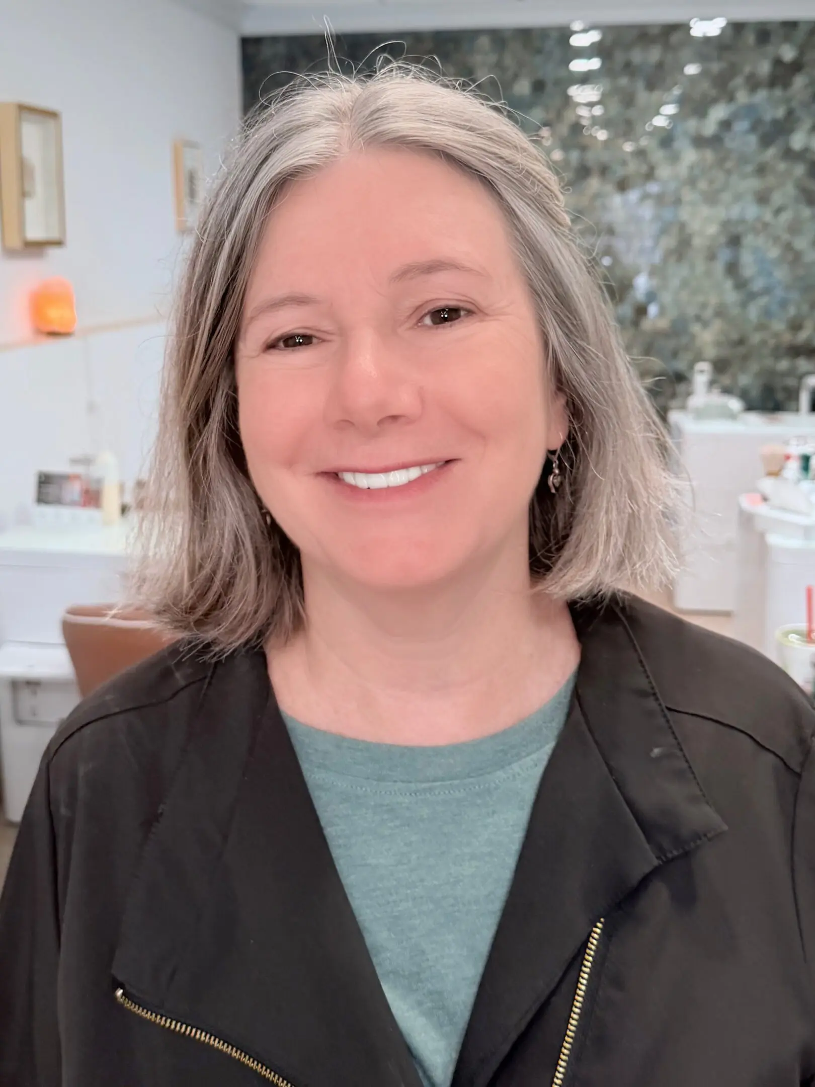 Smiling woman with shoulder-length gray hair in casual attire.